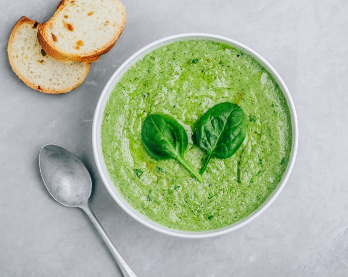 Green creamy spinach soup with baguette toasts on a gray concret